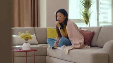 Battaniyeli kanepede oturan Asyalı hasta genç kadın kendini evinde hissediyor. Salgın. Coronavirus. Hastalıklı hastalık stresle karşı karşıya. Hastalık. Yavaş çekim