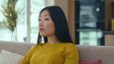 Asyalı genç ve çekici bir kadının gülümseyen portresi evdeki kanepede oturan kameraya bakıyor. Mutlu ol, başarılı ol. Seksi kızmış. Kapatın. Yavaş çekim