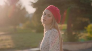 Şık, şık, beyaz elbiseli ve güneşli caddede yürüyen kırmızı bereli bir bayan. Resimli bir arka plan. Kadın modeli.