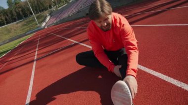Aktif yakışıklı beyaz adam koşudan sonra bacak kaslarını esnetiyor. Stadyumda yoga egzersizi yapıyor. Stadyum. Sporcu. Sağlıklı yaşam tarzı.
