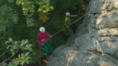 Uçurumdan inerken dikkat eden bir çift Kafkasyalı. Grup dağcıları ormanın derinliklerine tırmanıyor. Etkin yaşam biçimi.