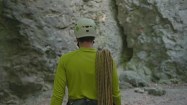 Ormanda genç sakallı bir adam miğfer takıyor ve güvenlik halatları takıyor kireçtaşı kayasına tırmanıyor. Uçurum tırmanışı. Olağanüstü aktivite sporları.