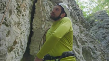 Ormandaki kireçtaşı kayalıklarına tırmanan bir adam. Sakallı dağcı, dağlara tırmanıyor, güvenlik ekipmanlarını ayarlıyor..