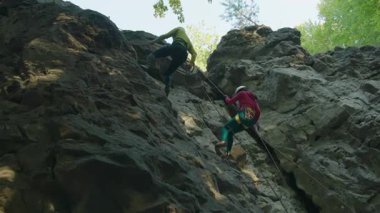 Dağcı çift dağlarda vakit geçiriyor. Dikkat et, erkek sporcular yüksek kayalardan aşağıya iniyorlar. Dağcılar. Yaz etkinliği.