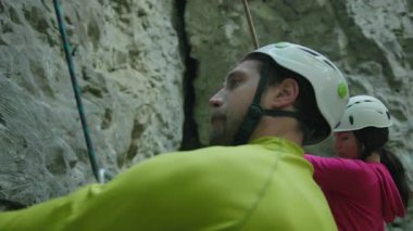 Kask takan genç sporcu ve sporcu bir çift dikkatlice dağa tırmanıyor. Yürüyüş aktivitesi. Ekstrem sporlar.