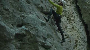 Aşırı yürüyüşçü, kasklı, sakallı, parlak sarı spor giyimli, kireçtaşı kayalıklara tırmanan genç adam..