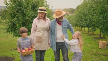 Mutlu son sınıf eşleri ve torunları meyve bahçesinde güneşli bir sonbahar gününün tadını çıkarıyorlar. Kırsal kesimde tatiller. Çiftlik kıyafetleri giymiş insanlar kameraya bakıp gülümsüyor. Kafkasyalı çocuk elinde elma sepeti tutuyor..