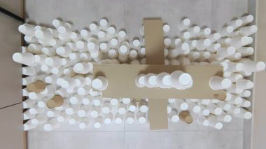 Beyaz kağıt bardak kulesinin üzerinden atlayan büyük gri kedinin zeminlerde ters dönmüş görüntüsü. Uluslararası yarışmalar için evcil hayvan hazırlıyorum. Sirk kedisinin sıradan hayatı..