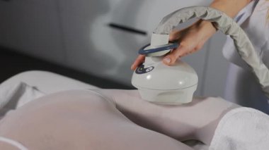 Aydınlık odada beyaz bir takım elbiseyle uzanmış, anti-selülit LPG masajı yaptırıyor. Kozmetoloji konsepti. Kilo kaybı. Vücut bakımı. Yavaş çekim