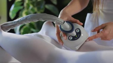 Kadın vücuduna anti-selülit LPG masajı yaparken ellerini kapat beyaz bir takım elbise içinde yan yatar. Kozmetoloji konsepti. Kilo kaybı. Vücut bakımı. Yavaş çekim