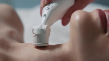 Kaplıca salonunda şarkı söyleyen ve boyun derisi tedavisi gören genç bir kadının yakın görüntüsü. Donanım prosedürü. Güzellik ve gençlik. Yenilenme, bakım, yenilenme, tıp