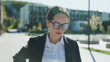 Gözlüklü genç ve güzel bir iş kadını öğle yemeği arasında yürüyor, cep telefonundan akıllı telefon alıyor. Resmi kıyafetler içinde güzel bir kız elinde cep telefonu, arkadaşıyla sohbet ediyor. Modern ofis binaları. Açık havada.