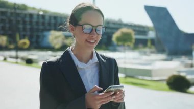 Zarif saç stili olan, akıllı telefon tutan, sohbet eden, seyir subayı kullanan, adres tabelası arayan sevimli beyaz bir kadının görüntüsü. Öğle yemeği saatinde toplantı. Modern parkın bulanık arka planı. Açık havada.