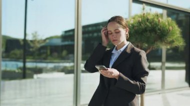 Elinde cep telefonu tutan, sosyal medyayı karıştıran, mesajlaşan, ciddi odaklanmış, genç, beyaz iş kadını fotoğrafı. Cam binanın yanında resmi giyinmiş bir kızın portresi. Dışarıda.