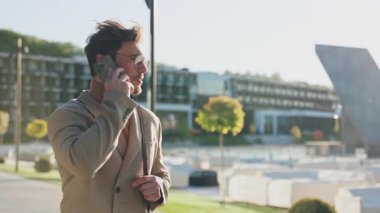 Yakın çekim gözlüklü genç adam telefonda konuşuyor. Sokakta yürürken etrafına bir bak. Güneş ışığı. Portre. Yavaş çekim