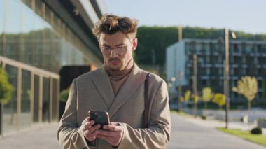 Sokakta gözlüklü yakışıklı bir adam yürürken telefon ekranına bakıp gülümsüyor. Sosyal medyayı karıştıran yakışıklı bir adam. Yavaş çekim