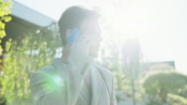 Modaya uygun bir adam, parlak güneş ışığıyla dışarıda duruyor. Parlak bir efektle sahneyi yıkıyor.