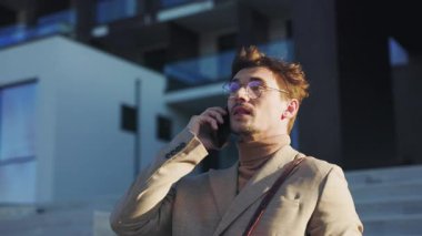 Modaya uygun bir işadamı, bir şirket binasının önünde önemli bir telefon görüşmesi yaparken görülüyor.