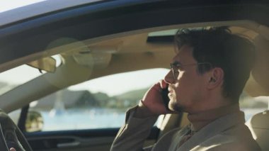 Derin düşüncelere dalmış bir adam liman boyunca araba sürerken sıcacık ve yumuşak güneş ışığıyla güzelce aydınlatılmış.