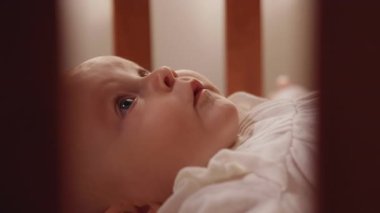 Minik bebek gülümseyen bir portre beşikteki beşikte sırtüstü yatıp etrafa bakıyor. Sevimli, oynak çocuk. Kapatın. Ağır çekim. Yüksek kaliteli FullHD görüntüler