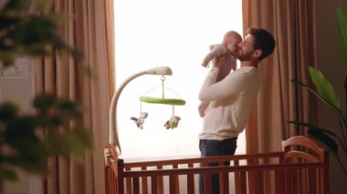 Sakallı genç baba, yeni doğmuş bebeğine nazikçe sarılıyor. Birlikte oynuyoruz. Evdeki modern dairelerde duruyor. Mutlu ol. Kapatın. Yavaş çekim