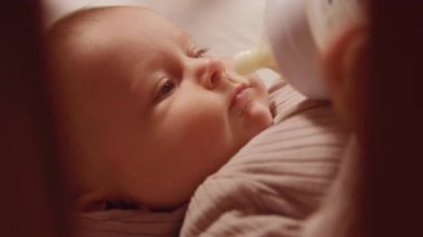 Yatakta yatan şişeden yemek yiyen yeni doğmuş bir çocuğa yakın çekim. Anne bebeği besliyor. Şirin. Dikkat et. Süt içmek. Portre. Yavaş çekim