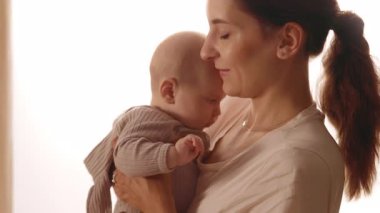 Evde mutlu bir anne kucağında ve yeni doğmuş bebeği okşuyor. Gülümsüyor. Apartmanda dikiliyorum. Annelik. Portre. Yavaş çekim