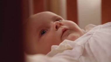 Beyaz elbiseli şirin bir bebeğin tahta karyolada yatışının yakın çekim görüntüleri. Kafkas bebeğinin komik portresi. İçeride. Ebeveynlik kavramı. Ev