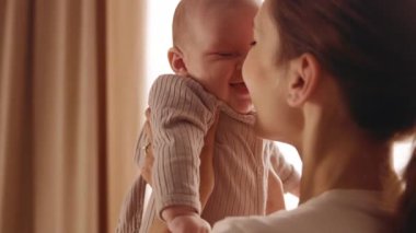 Anne ve bebeğin vurulması. Yeni doğmuş bebeği kollarında tutan ve onu öpen mutlu genç kadın. Sevimli çocuk gülümsüyor ve gülüyor. Ev, aile, annelik.