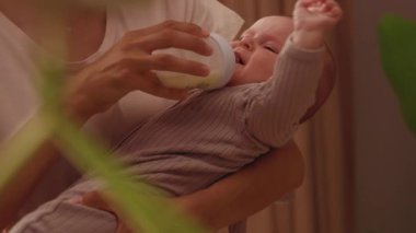 Anne kucağında mutsuz bir çocuğu süt şişesinden besliyor. Yeni doğmuş şirin bir bebeğin portresi. Sevgi dolu bir kadın ve oğul. Çocuk bakımı. Sıcak çocuk odası. Ev, ev. Aile