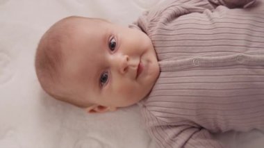 Çocuk beşiğinde sırıtan, gülümseyen, etrafa bakınan komik bir bebek resmi. Portre sanatçısı çocuk. Kapatın. Yavaş çekim