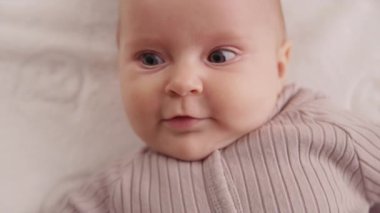 Çocuk beşiğinde sırıtan, gülümseyen, etrafa bakan küçük bebeğin sevimli yüzü. Portre sanatçısı çocuk. Kapatın. Yavaş çekim