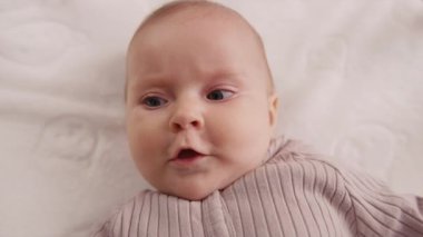 Yeni doğmuş bebeğe gülümseyen, beşikte sırtüstü yatıp etrafa bakan. Portre sanatçısı çocuk. Kapatın. Yavaş çekim