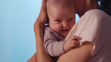 Yakın çekim annesi kollarını tutuyor ve akşamları gülümseyen komik bebekleri okşuyor. Dairede mutlu oldum. Annelik. Portre. Yavaş çekim