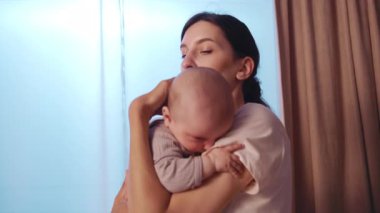 Komik, genç ve mutlu annenin portresi kucağında ve yeni doğmuş bebeği okşuyor. Akşamları gülümsüyor. Apartmanda dikiliyorum. Annelik. Portre. Yavaş çekim