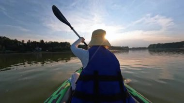 Gün batımında gölde kayak yapan bir kadını çek. Kanoda kürek çeken bir kız. Su, doğa, spor, aktif turist, kano kiralama, turizm