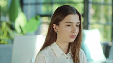 Ciddi bir çalışan genç kadın güneş ışığı ofisindeki bir kameraya bilgisayarla bakıyor. Modern çalışma alanı. Teknoloji. İş kadınları işte. Ofis çalışanı. Yavaş çekim