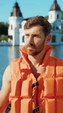 Turuncu can yeleği giyen bir adam, tarihi mimariyle çevrili bir gölün sakin sularından zevk alır..