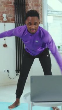 Genç bir adam dizüstü bilgisayarını kullanarak mutlu bir şekilde esniyor. Parlak ve aydınlık bir iç mekan.