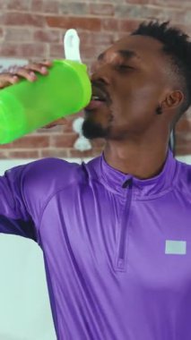 Odaklanmış bir adam besleyici bir protein karışımından zevk alır. Modern bir spor salonunda spor ve sağlığa olan güçlü bağlılığını gösterir.