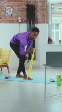 Genç bir adam evde spor yapıyor. Parlak ve şık bir yerde direniş bandı kullanıyor.