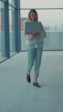 Kendine güvenen bir iş kadını dizüstü bilgisayarını taşırken kasıtlı olarak modern ofis ortamında adım atar.