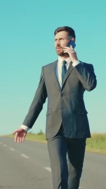 İyi giyimli takım elbiseli bir işadamı ıssız bir yolda kasıtlı olarak yürüyor ve bir telefon görüşmesi yapıyor.