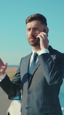 Mükemmel bir takım elbise giymiş iyi giyimli bir işadamı çarpıcı bir manzaranın yanında acil bir telefon görüşmesi yapıyor.