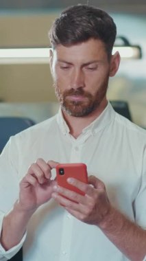 Genç bir adam, modern ofis ortamında, çağdaş yaşamı gösteren akıllı telefonuyla derinden ilgilenir.