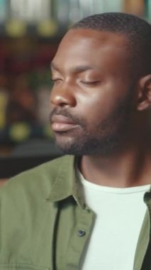 Gündelik giysiler giymiş bir adam canlı ve renkli bir ortamla çevrili iken düşünceli bir şekilde yan tarafa bakar.