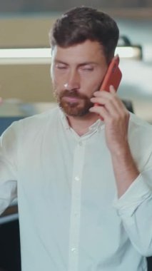 Gıcır gıcır beyaz gömlek giyen bir adam, dinamik bir çalışma ortamını gösteren bir telefon görüşmesi yapıyor.