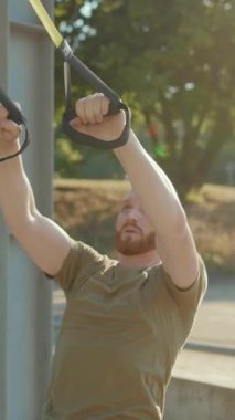 Bir adam güneşli bir açık hava ortamında süspansiyon tatbikatı yapıyor, spor salonu ve güç gösterisi yapıyor..