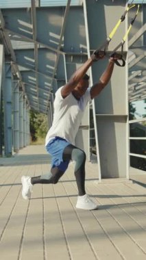 Bir adam açık hava TRX eğitim oturumunda olağanüstü gücünü ve formda olduğunu gösteriyor.