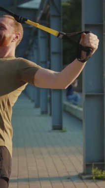 Bir adam TRX süspansiyon kayışlarını ustalıkla kullanırken eğlenceli ve keyifli bir spor seansından zevk alıyor.